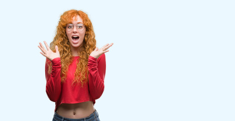 Young redhead woman wearing glasses very happy and excited, winner expression celebrating victory screaming with big smile and raised hands