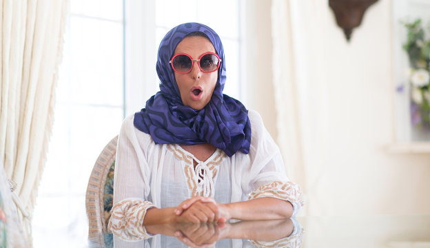 Middle age brunette arabian woman wearing colorful hijab at luxury house scared in shock with a surprise face, afraid and excited with fear expression