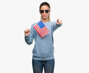 Fototapeta premium Beautiful young woman holding USA flag pointing with finger to the camera and to you, hand sign, positive and confident gesture from the front