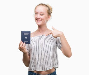 Blonde teenager woman holding passport of Germany with surprise face pointing finger to himself