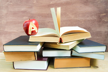 Back to school and knowledge concept. Stack of books and fresh red apple with mark A on wooden background