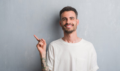 Young adult man standing over grey grunge wall very happy pointing with hand and finger to the side