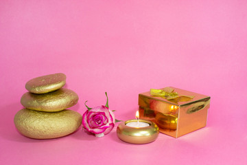 Gift set. Candle, stones, gift box, and rose. On a pink background.