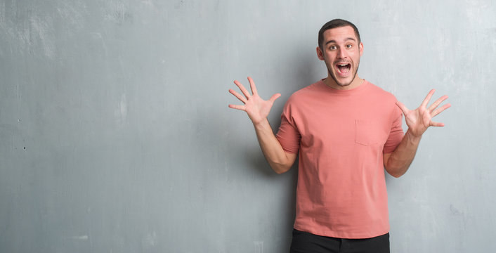 Young caucasian man over grey grunge wall celebrating crazy and amazed for success with arms raised and open eyes screaming excited. Winner concept