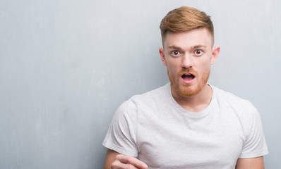 Obraz premium Young redhead man over grey grunge wall scared in shock with a surprise face, afraid and excited with fear expression