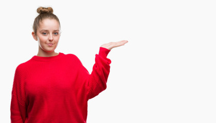 Young blonde woman wearing bun and red sweater smiling cheerful presenting and pointing with palm of hand looking at the camera.