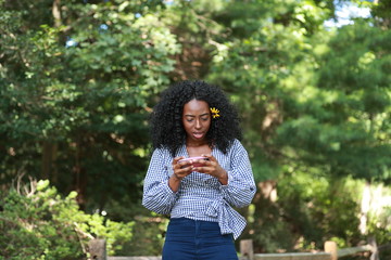 Stylish black woman using phone in green park