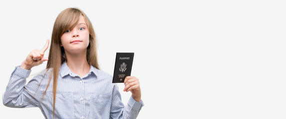 Young blonde toddler holding american passport surprised with an idea or question pointing finger with happy face, number one