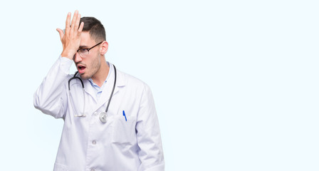 Handsome young doctor man surprised with hand on head for mistake, remember error. Forgot, bad...