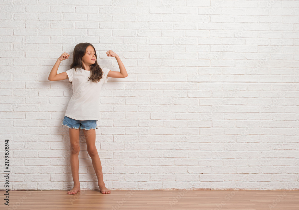 Wall mural young hispanic kid stading over white brick wall showing arms muscles smiling proud. fitness concept