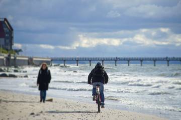 An elderly woman walks along the sandy beach towards the cyclist.