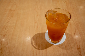 Fruit black tea with ice cube in tall glass on table.