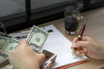 Hand of businessman holding pen to write business document and contact sheet near black coffee with warm morning light near the window.Copy space.