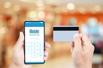 Hand holding smartphone with Mobile Banking on screen over blurred in shopping mall background for online payment via credit card