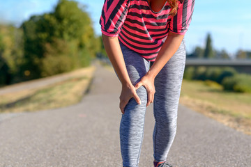 Woman wearing sporstwear holding her painful knee