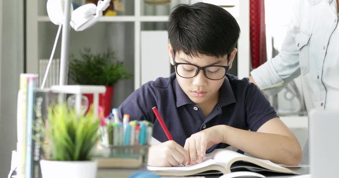 Cute asian mother helping your son doing your homework at home with smile face together.