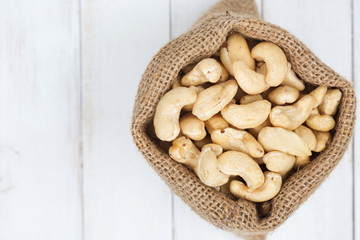 Pile of cashew nuts in sackcloth pouch on white wooden desk.