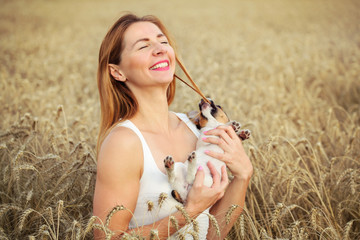 Woman with Jack Russell terrier puppy on her hands, wheat field in background, dog is restless and...