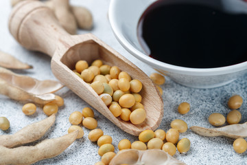 Soybeans in wooden spoon, pods and soy sauce in a white bowl on a gray concrete surface