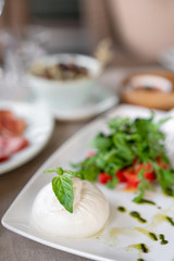 Italian Caprese salad. burrata cheese, tomatoes and basil herb leaves. Balsamic vinegar arranged on white plate