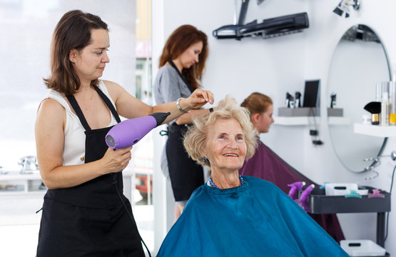 Stylist using hair dryer for senior woman