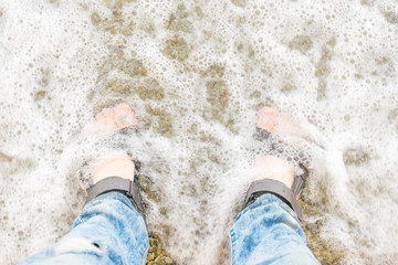 Male feet in sandals in the water at the beach.