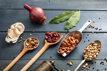 Top view of flat lay of assortment of pulses legumes on black wooden tabletop background, in scoop and ladles and grater.