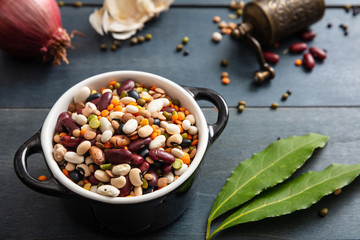 Flat lay of assortment of legumes pulses on black wooden tabletop background, in enamel bowl