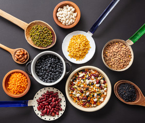 Top view of flat lay of assortment of legumes pulses on black tabletop background, in scoop,...