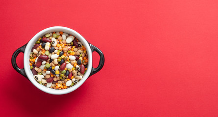 Assortment of legumes pulses in enameled bowl on red background, isolated, top view, copy space.