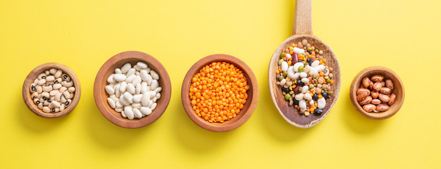 Assortment of legumes pulses in wooden bowls on yellow, background, isolated, top view, banner.