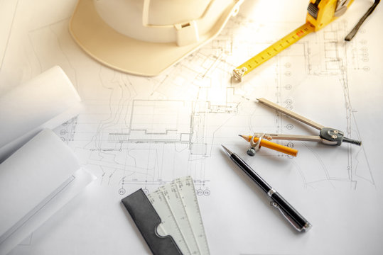Compass tool, pen, scale, tape measure and safety helmet on architectural drawing plan of house project, blueprint rolls on working table, Architecture and building construction industry concepts