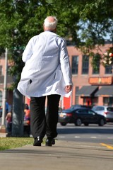 Senior Balding Male Doctor Walking On Sidewalk