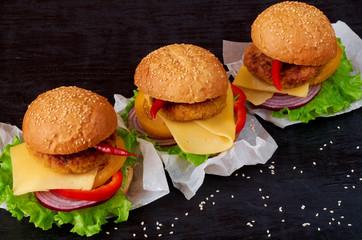 Tasty burgers with falafel, salad, onion rings, cheese, tomatoes and sesame on the black background. Classic american veggie fast food. Side view