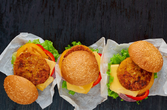 Three vegetarian burgers with falafel, salad, onion rings, cheese and tomatoes on the black background. Traditional Middle Eastern fast food. Top view with copy space for text