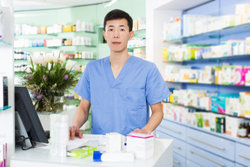 japanese specialist standing near table with cashbox in pharmacy