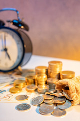 Table clock and gold coin stack on the table with international banknotes currency. Time investment and passing time. Urgency countdown timer for business deadline concept