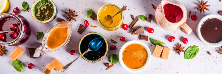 Various sweet sauces, toppings and syrups - lemon, orange, caramel, chocolate, cranberry, cherry, blueberry, on a light concrete background, top view copy space for text banner