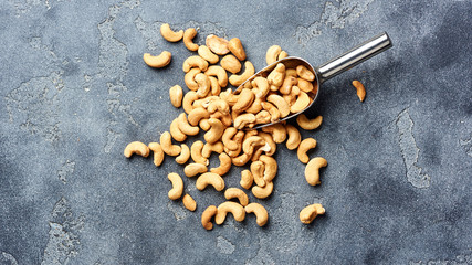 Roasted cashew nuts and scoop on gray background. Top view.