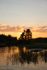 Sunset on the lake in the forest. Beautiful sunset. The sun goes behind the top of the trees on the lake.