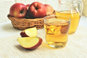 Apple juice in a glasses and raw red apples on a table.