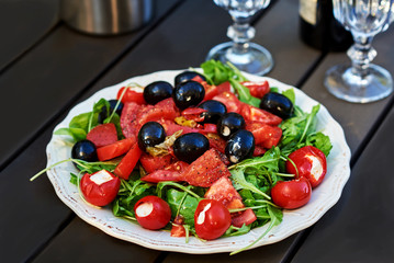 Fresh salad with tomatoes, spinach, arugula,  in a plate on rustic wooden background.