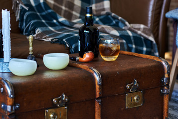 Bottle and glass of whiskey with ice on a wooden old suitcase.