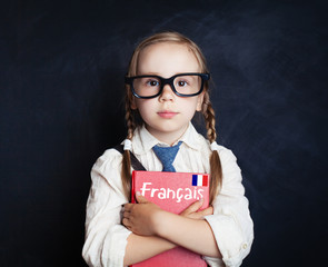 Kids learn French. Smart child girl with French book and flag on chalkboard in language school