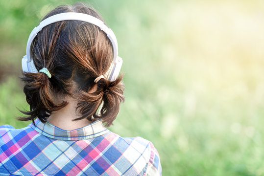 Girl with headphones view from behind in the nature, sunny