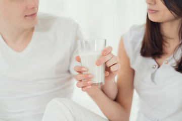 couple in white clothes holding a glass with milk, close-up