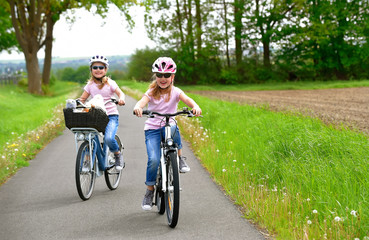 Fototapeta premium Twin sisters ride their bicycles with scenic landscape around them. They have happy smiling faces on them as they enjoy the outdoor cycle tour.