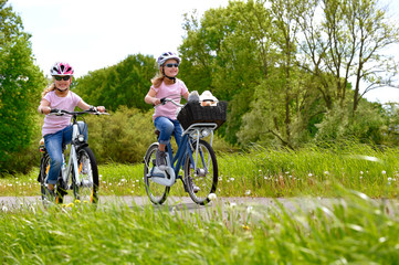 Fototapeta na wymiar Twin sisters ride their bicycles with scenic landscape around them. They have happy smiling faces on them as they enjoy the outdoor cycle tour.