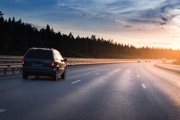 Highway traffic in sunset. minivan on the asphalt road with metal safety barrier or rail. Pine...