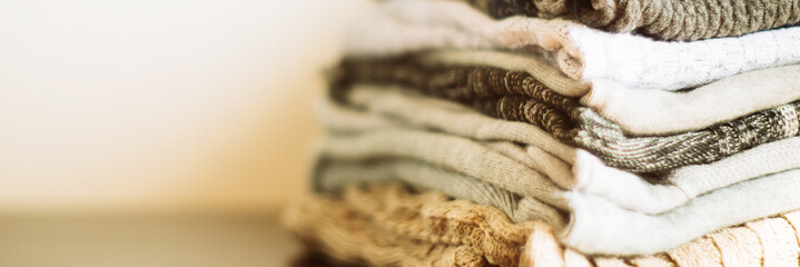 Stack of cozy knitted clothes on a wooden stand. banner, long wide